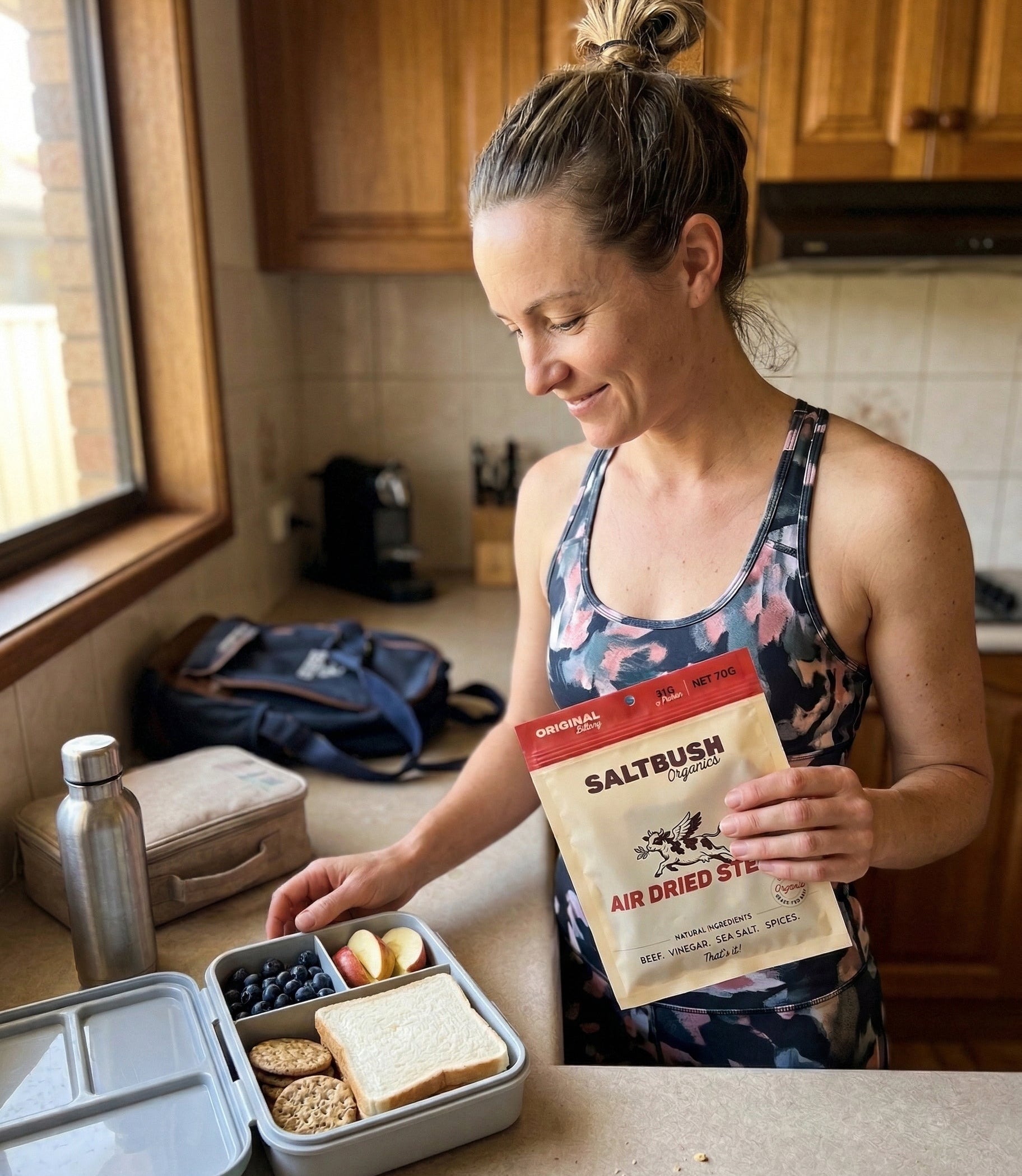 Woman in a kitchen holding a package of Saltbush Air Dried Steak with a bento box on the counter.